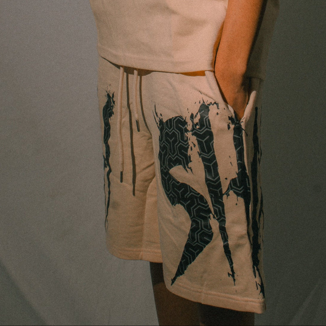 Person wearing a beige t-shirt and shorts with black graphics against a plain background